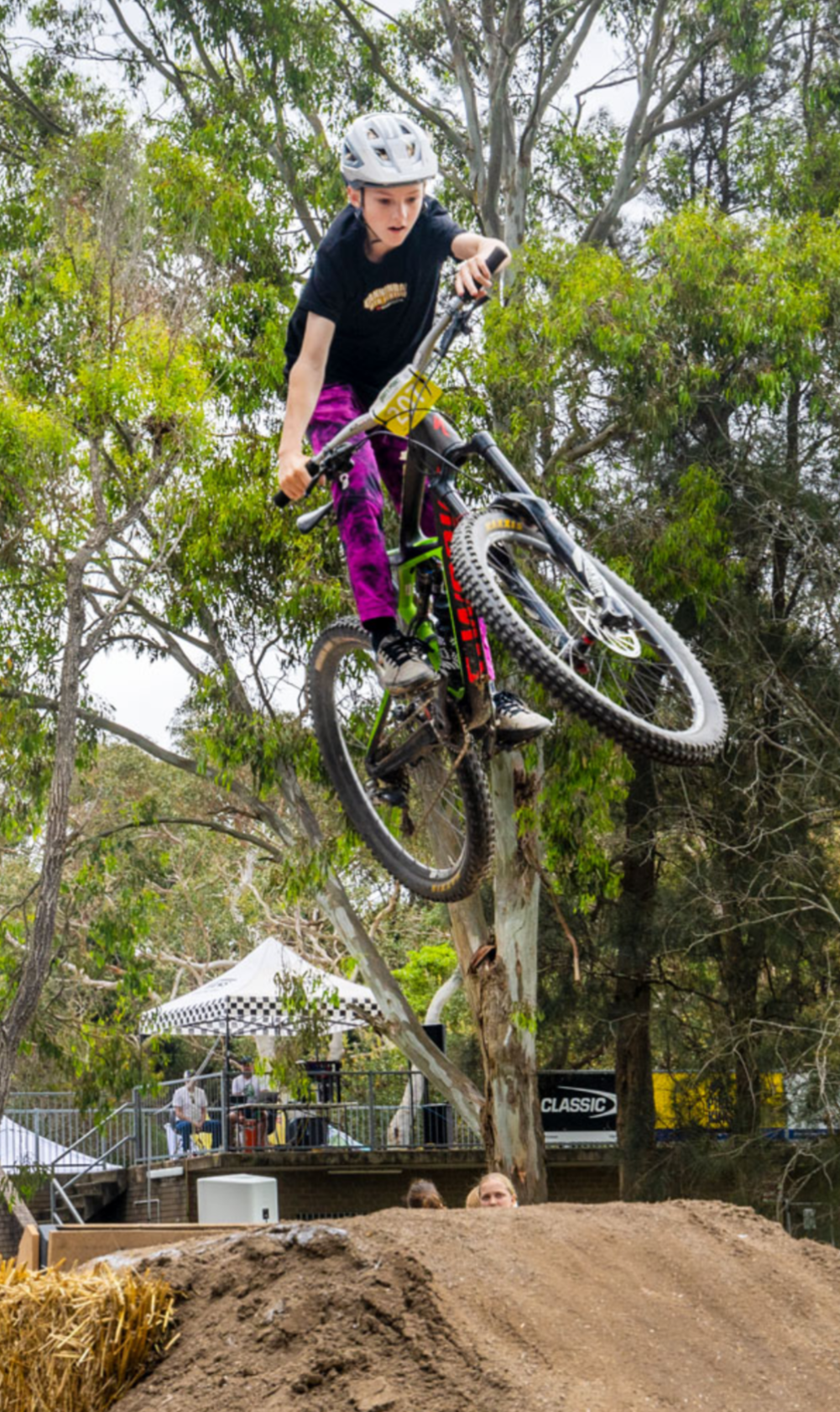 Person on a bicycle performing a jump in a forested area with trees and a clear sky.